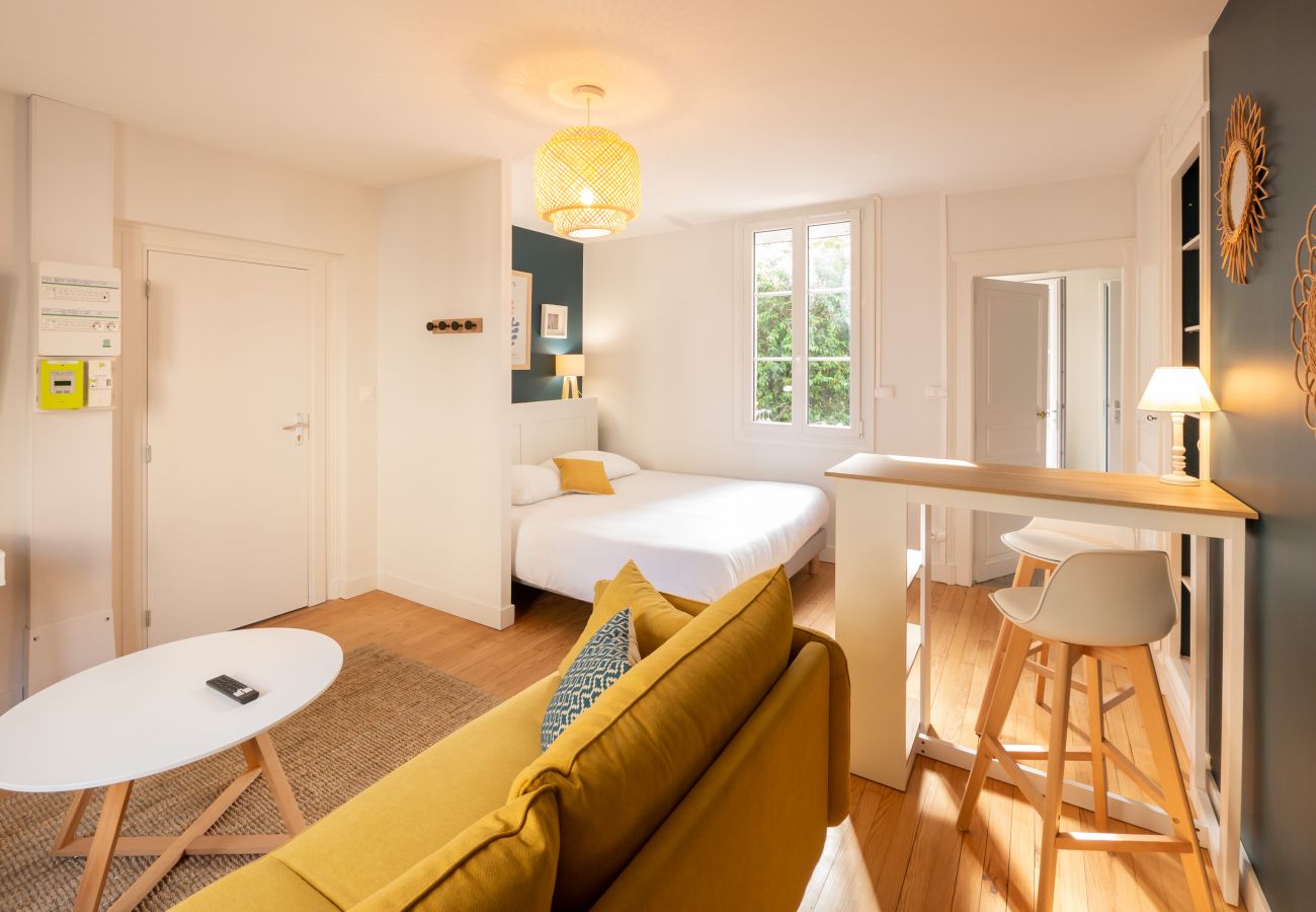 Studio avec salon comprenant canapé, table basse et télévision, coin chambre avec lit double, espace repas avec mange-debout