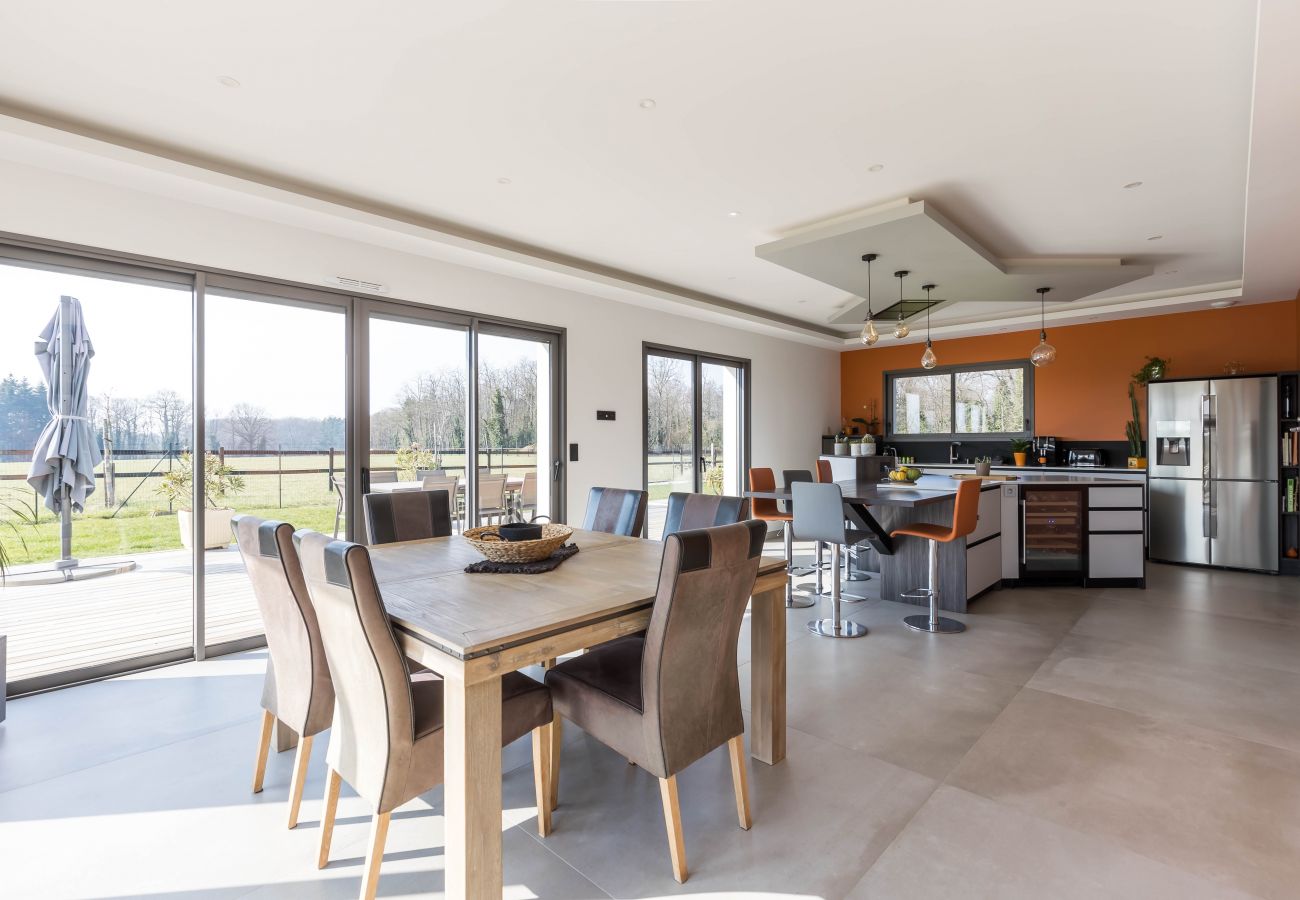 Table à manger en bois avec chaises confortables, cuisine moderne et vue sur la terrasse et le jardin