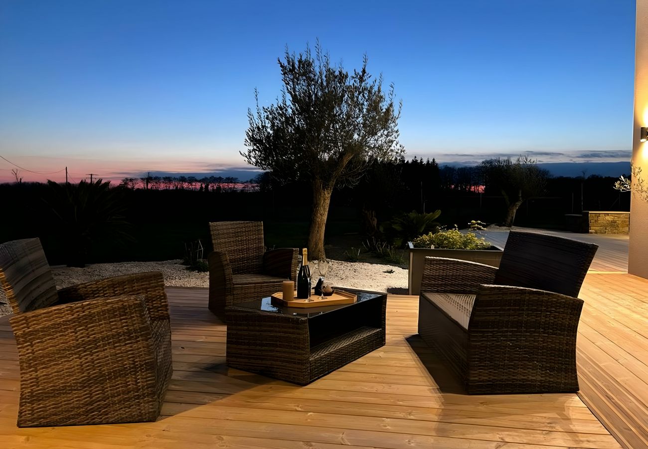 Terrasse bien éclairée avec sièges en osier et table basse, offrant une vue sur le jardin et l'horizon